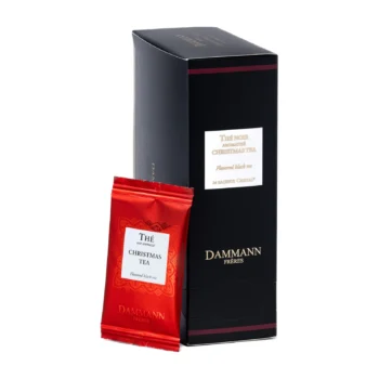 Boîte noire élégante de thé noir Dammann Frères Christmas Tea avec un sachet cristal rouge individuel posé devant.