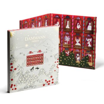 Calendrier de l'Avent Dammann Frères 2025 orné d'une illustration de maison enneigée et d'arbres de Noël, avec un aperçu d'un design intérieur rouge festif