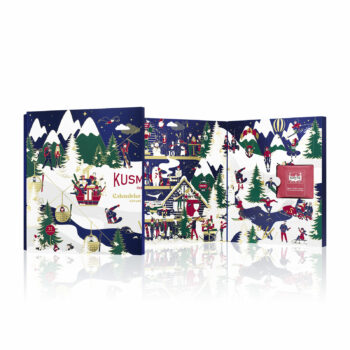 Calendrier de l’Avent Kusmi Tea 2024 partiellement ouvert, révélant une boîte miniature de thé dans l'une des cases. Le design extérieur montre un paysage de montagne enneigée avec des sapins et des personnages célébrant les fêtes de fin d'année.