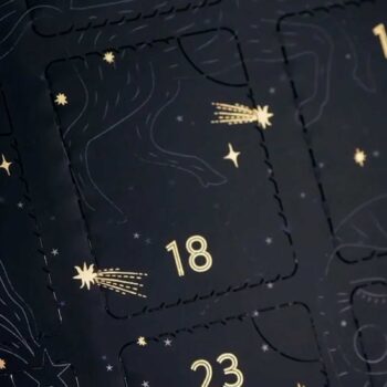 Calendrier de l'avent noir avec des étoiles et des comètes dorées, mettant en évidence les cases numérotées dix-huit et vingt-trois