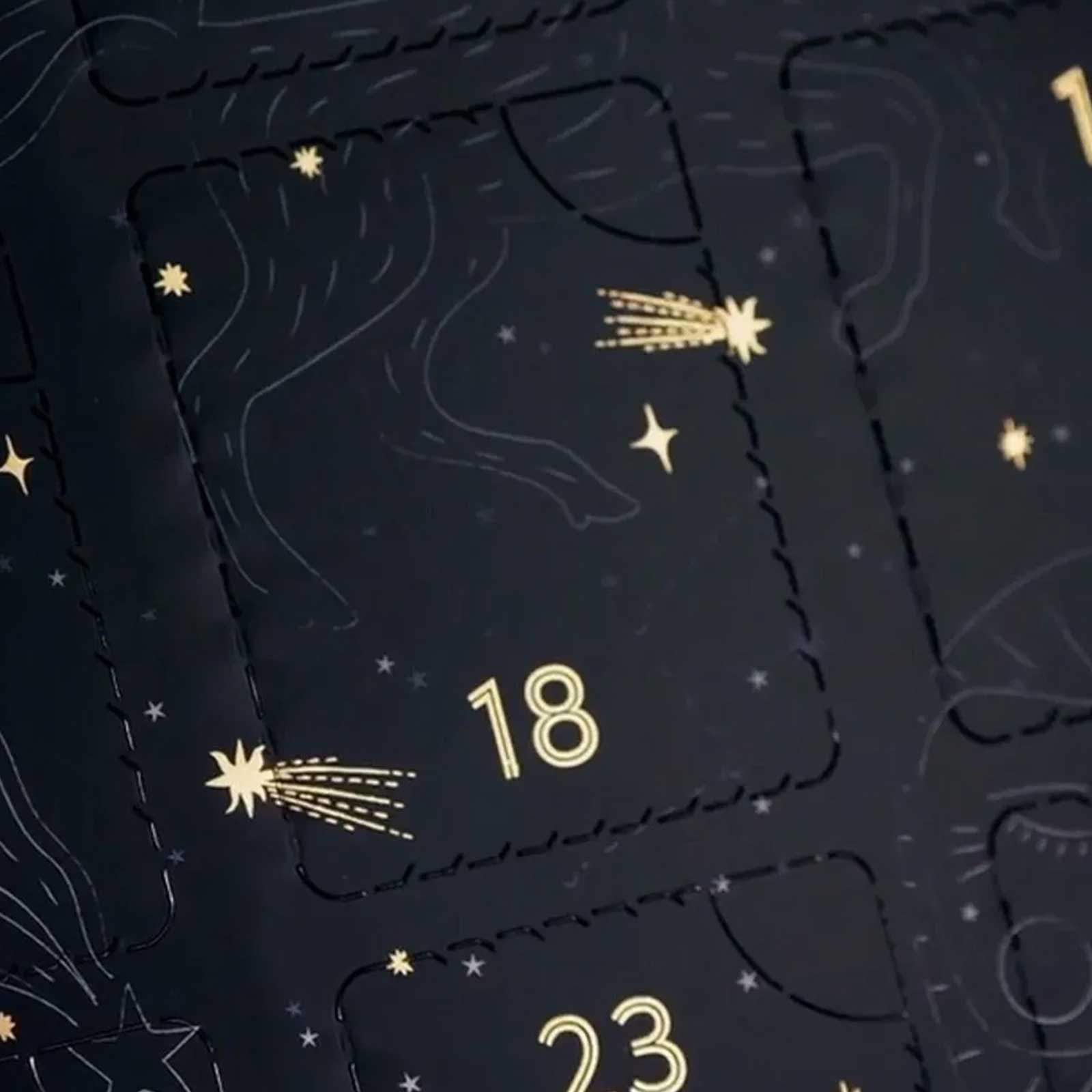 Calendrier de l'avent noir avec des étoiles et des comètes dorées, mettant en évidence les cases numérotées dix-huit et vingt-trois