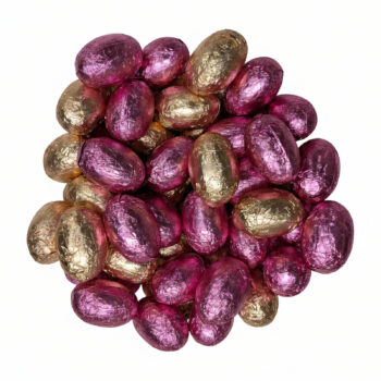 Gros plan sur un tas d'œufs de Pâques pralinés assortis, certains en emballage rose vif (chocolat au lait) et d'autres en emballage doré (chocolat noir), sur fond blanc.