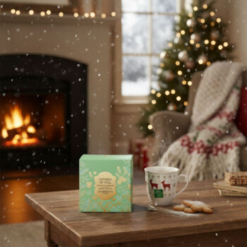 Boîte verte dorée de tisane de Noël Dammann Frères sur une table en bois, devant une tasse ornée de rennes et des biscuits de Noël