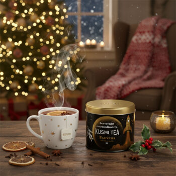 Boîte de thé Kusmi Tea Tsarevna édition 2024 bio, avec une tasse fumante de thé aux épices et une décoration de Noël en arrière-plan.
