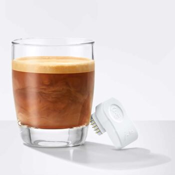 Verre de café espresso avec une crema épaisse, à côté d'un adaptateur Wi-Fi Connect Jura blanc