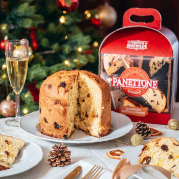 Panettone de Le Comptoir de Mathilde, un pain brioché aux raisins et zestes d'orange, servi avec une coupe de champagne, décorations de Noël en arrière-plan