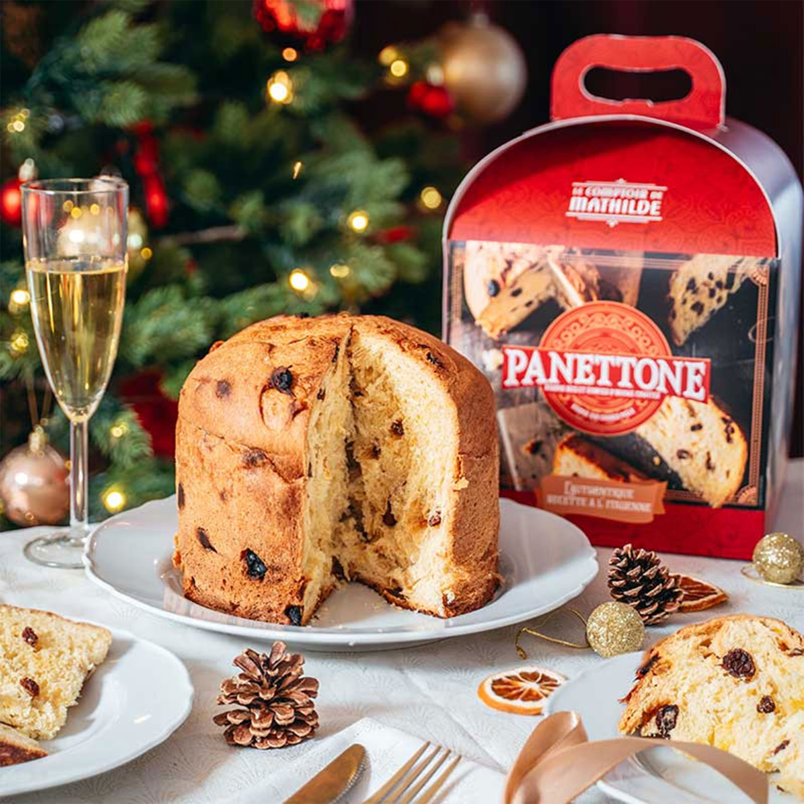 Panettone de Le Comptoir de Mathilde, un pain brioché aux raisins et zestes d'orange, servi avec une coupe de champagne, décorations de Noël en arrière-plan