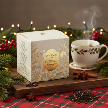 Boîte de Christmas Tea Dammann Frères sur un plateau en bois, entourée de décorations de Noël, avec une tasse de thé fumante à côté.