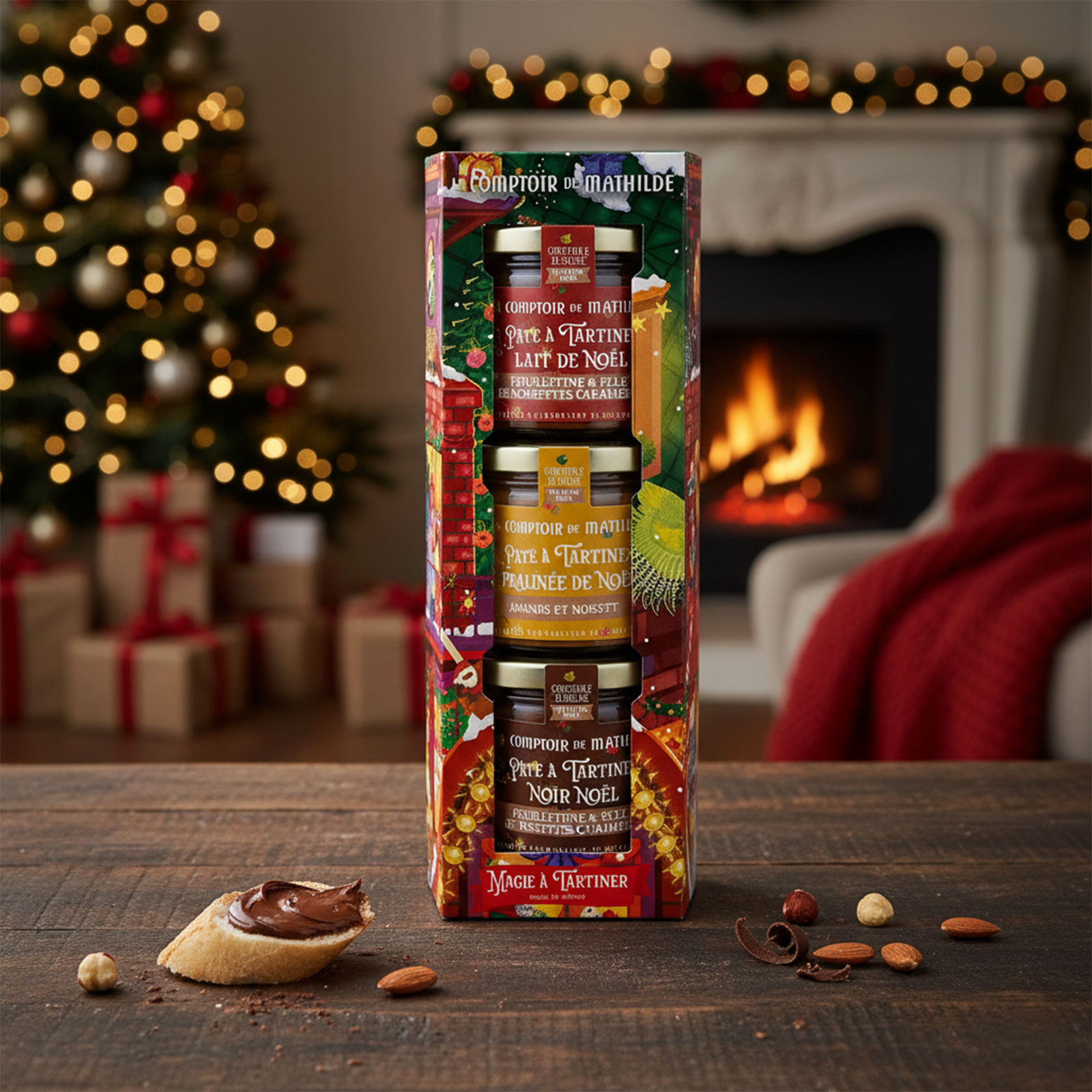 Coffret cadeau Le Comptoir de Mathilde avec trois pots de pâtes à tartiner de Noël sur une table en bois, une tranche de pain tartinée de chocolat à proximité