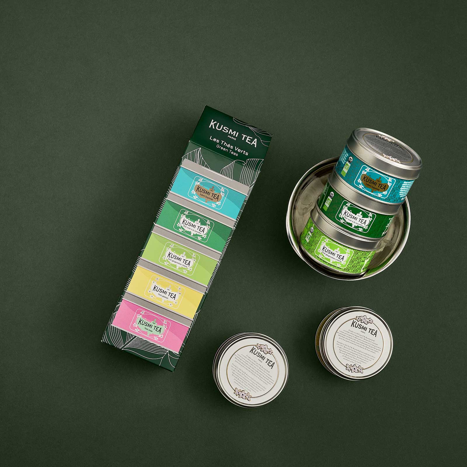 Coffret de thés verts Kusmi Tea composé de cinq boîtes métalliques colorées empilées et de trois boîtes individuelles disposées sur un fond sombre