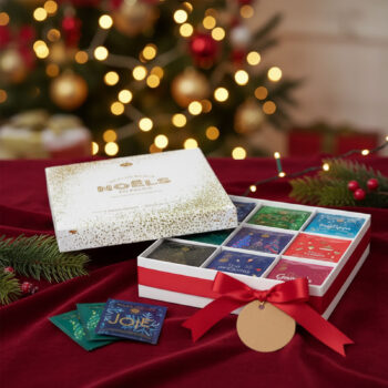 Coffret cadeau de Noël 'Les plus beaux Noëls du Palais' ouvert, révélant 9 variétés de thés festifs en sachets, décoré d'un ruban rouge et d'un sapin scintillant en arrière-plan.