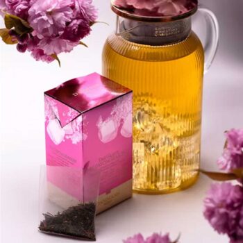 Boîte de thé glacé Dammann Frères Blossom Season rose avec un sachet de thé vert et une carafe de thé glacé remplie de glaçons et de fleurs de cerisier