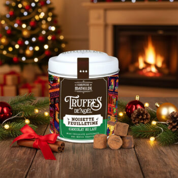 Boîte métallique festive "Truffes de Noël" Le Comptoir de Mathilde, garnie de truffes au chocolat au lait, noisettes et feuilletine, décorée d'un village illuminé.