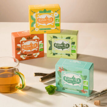 Boîtes de thé Kusmi Tea aux saveurs Pomme-Cannelle, Thé-Citron-Camomille, Verveine-Menthe et Réglisse-Menthe, avec une tasse de thé et des bâtons de réglisse