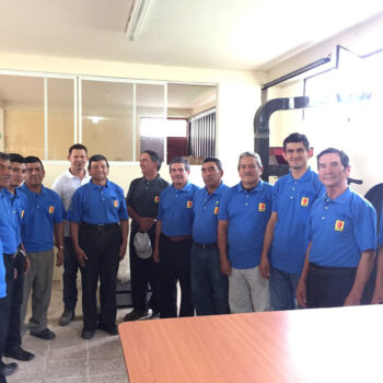 Groupe de producteurs de café en tenues bleues uniformes, posant ensemble dans une salle lumineuse. Ils représentent la coopération et l'esprit collectif au sein de la coopérative FAPECAFES, qui soutient les petits producteurs locaux.