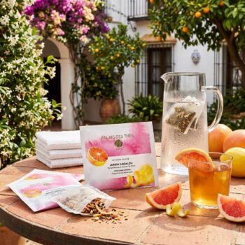 Sachets de thé glacé Jardin Andalou de Palais des Thés, avec des tranches de pamplemousse et de citron, un pichet d'eau et un verre de thé glacé