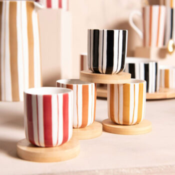 Quatre gobelets en porcelaine à rayures verticales rouges, oranges, jaunes et noires, posés sur des sous-verres en bois