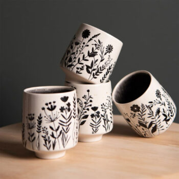 Quatre gobelets en porcelaine blanche décorés de motifs floraux noirs, empilés sur une table en bois