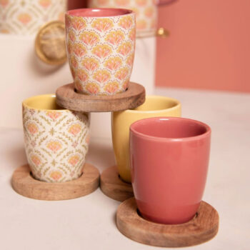 Six gobelets en grès avec des motifs floraux colorés et des sous-tasses en bois, présentés en groupe