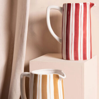 Deux pichets rayés, l'un rouge et blanc, l'autre ocre et blanc, présentés sur des blocs décoratifs, évoquant le design floral inspiré du Japon
