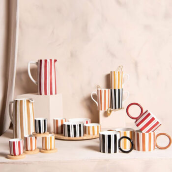 Collection de tasses et de pichets rayés aux couleurs vives, disposés sur un fond pastel, évoquant une ambiance joyeuse et printanière.