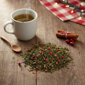 Mélange de thé vert Dammann Frères avec des baies rouges, des bâtons de cannelle et une tasse de thé fumant sur une table en bois.