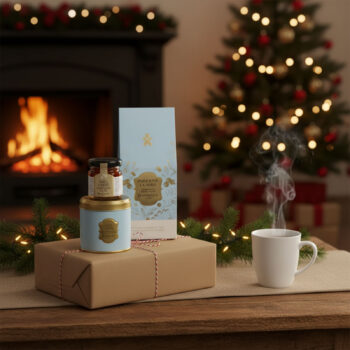 Coffret cadeau Dammann Frères pour Noël avec une pochette de thé Paris sous la neige, une mini boîte de thé, une gelée de thé et une tasse fumante, près d'une cheminée et d'un sapin de Noël.