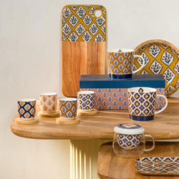 Ensemble de tasses et mugs en porcelaine avec des motifs géométriques bleus et ocres sur fond blanc, disposés sur une table en bois.