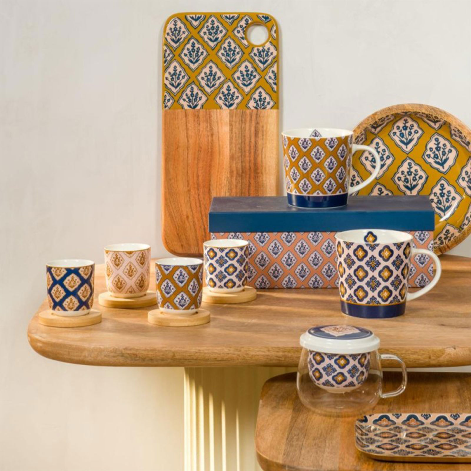 Ensemble de tasses et mugs en porcelaine avec des motifs géométriques bleus et ocres sur fond blanc, disposés sur une table en bois.