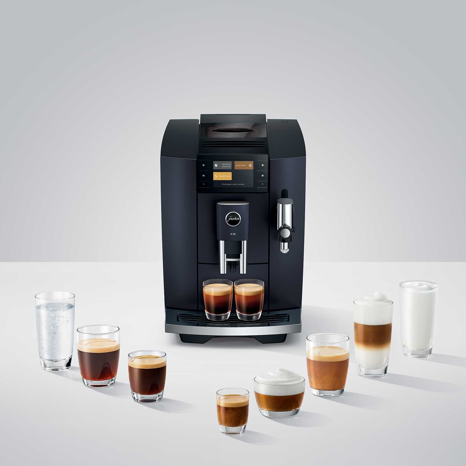 Machine à café JURA E8 Cosmic Black entourée de verres de différentes préparations de café, dont des expressos, cappuccinos et un verre d'eau