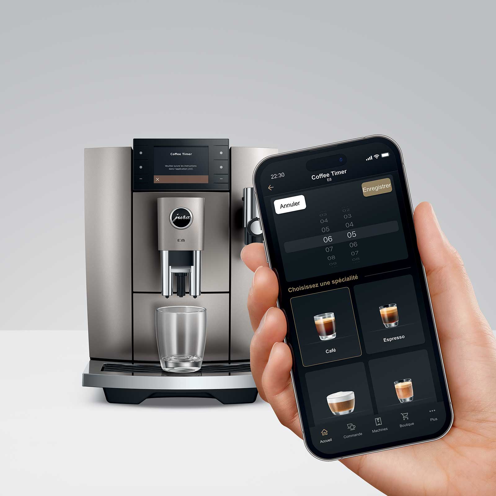 Une machine à café Jura E8 argentée, avec un smartphone tenu en main affichant l'application J.O.E. et la fonction Coffee Timer pour programmer les boissons