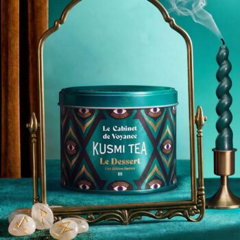 Boite de thé bio Kusmi Tea Le Cabinet de Voyance posée devant un miroir rétro avec des pierres divinatoires au premier plan et une bougie allumée