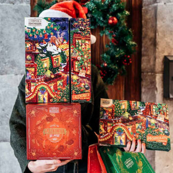 Personne tenant des calendriers de l'avent festifs du Comptoir de Mathilde remplis de chocolats chauds, décorations de Noël en arrière-plan