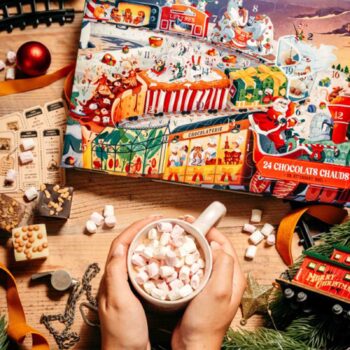 Mains tenant une tasse de chocolat chaud avec des guimauves devant un calendrier de l'avent festif sur une table en bois décorée