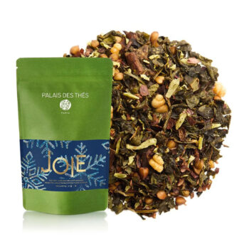 Sachet vert de Thé vert Joie Bio de Palais des Thés à côté d'une pile généreuse de thé en vrac, mélange de feuilles vertes, de morceaux de fruits et de noix.