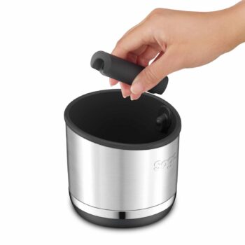 Main tenant une barre d'éjection noire amovible au-dessus d'un bac à marc de café en acier inoxydable Sage