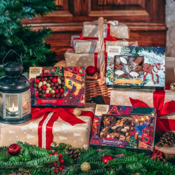 Coffret Le Comptoir de Mathilde Mendiants de Noël sur un fond de sapin et de cadeaux, illustrant des chocolats avec fruits secs.