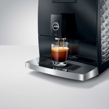 Machine à expresso JURA C9 Piano Black versant un café crémeux dans un verre transparent, logo Jura visible