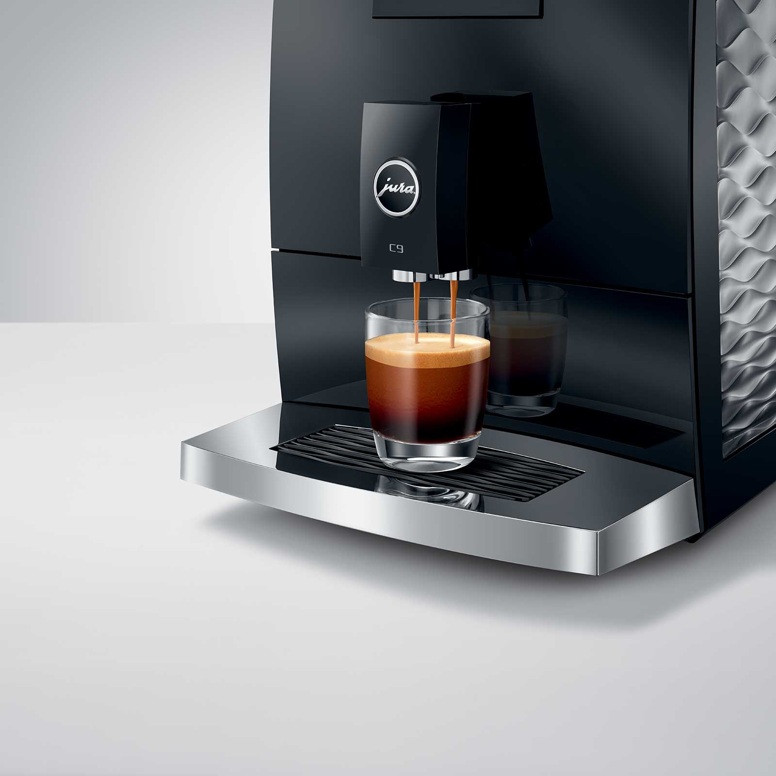 Machine à expresso JURA C9 Piano Black versant un café crémeux dans un verre transparent, logo Jura visible