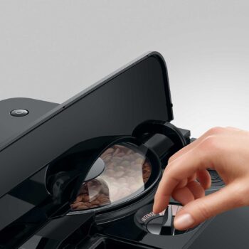 Main ajustant le bouton d'intensité sur une machine à café JURA C9, avec des grains de café visibles dans le compartiment transparent