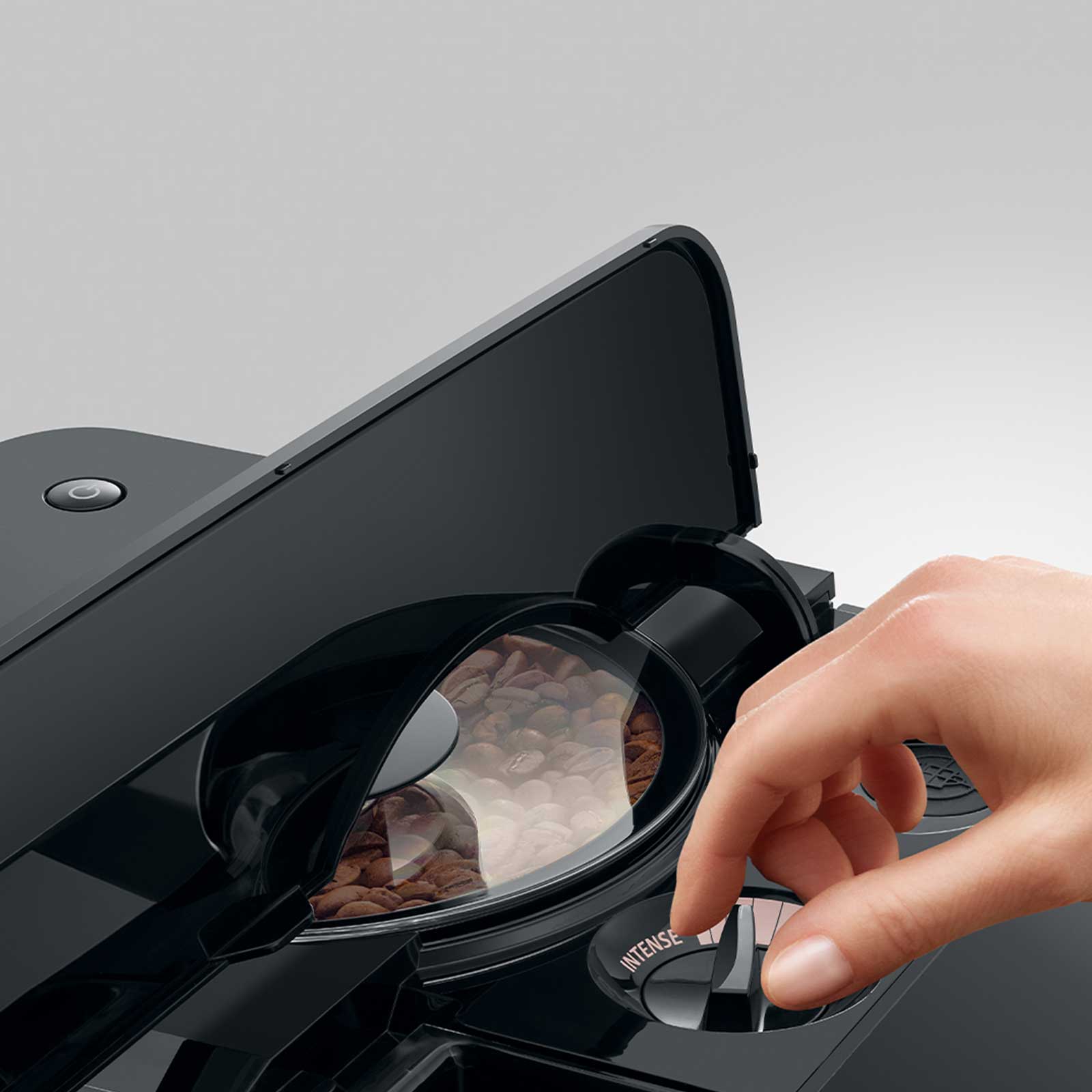 Main ajustant le bouton d'intensité sur une machine à café JURA C9, avec des grains de café visibles dans le compartiment transparent
