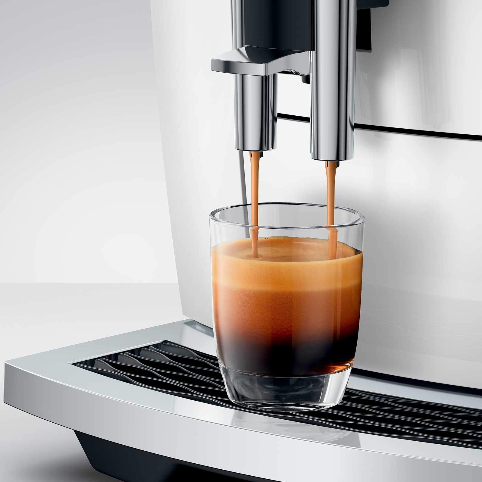 Machine à expresso JURA E8 Piano White versant un café crémeux dans un verre transparent, avec deux jets de café