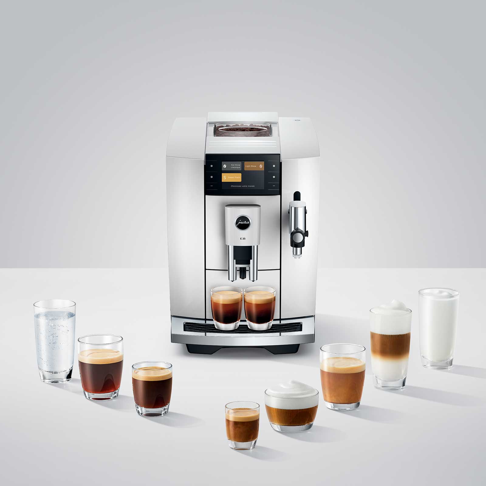 Machine à café JURA E8 Piano White entourée de verres de différentes boissons au café et d'un verre d'eau.