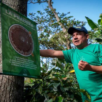 Homme présentant une affiche explicative sur la culture du café à la ferme La Pradera, Colombie, avec des détails sur les zones de culture et les processus.