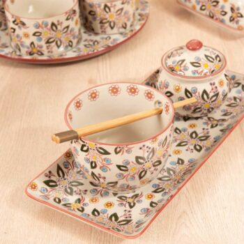 Bol en grès avec motifs floraux colorés, baguettes en bois naturel posées dessus, sur un plateau assorti