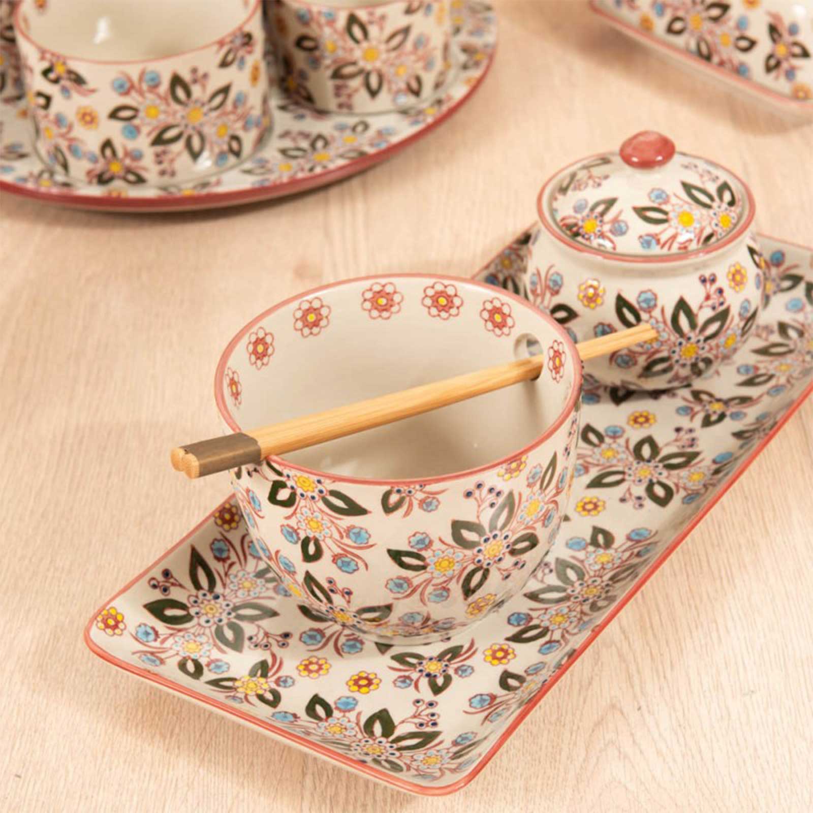 Bol en grès avec motifs floraux colorés, baguettes en bois naturel posées dessus, sur un plateau assorti
