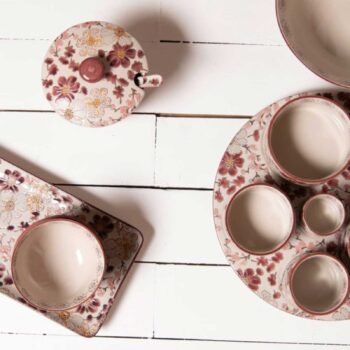 Ensemble de vaisselle Kiyo avec bol, couvercle et cuillère, décor floral bordeaux et rose sur fond crème, sur table en bois blanc