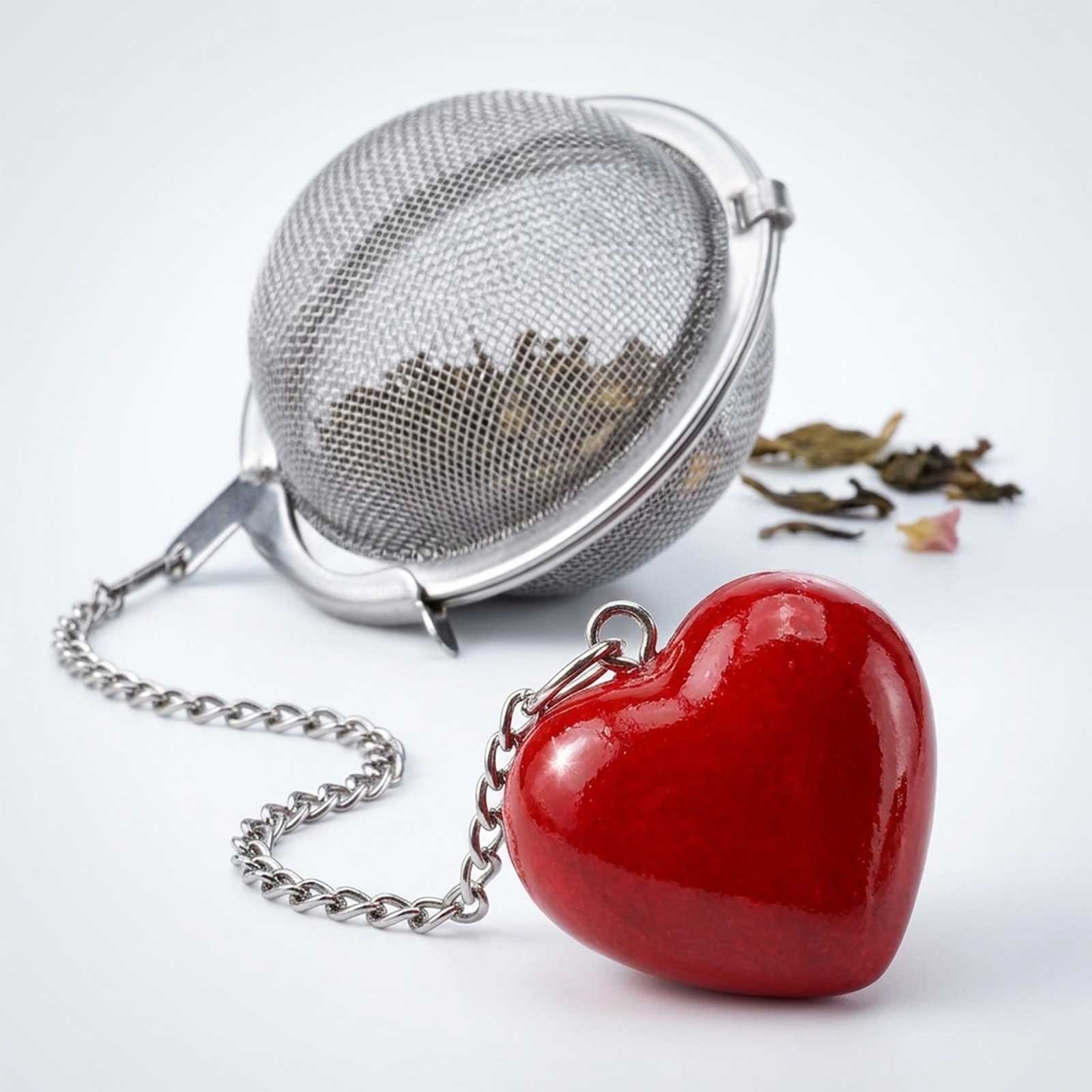 Boule à thé en acier inoxydable avec un pendentif en forme de cœur rouge vif, remplie de feuilles de thé séchées