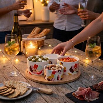 Plateau en bois Amadeus Alexia avec quatre bols en céramique décorés de fleurs colorées, remplis d'olives, de noix et de houmous, sur une table en bois avec des crackers et du jambon.