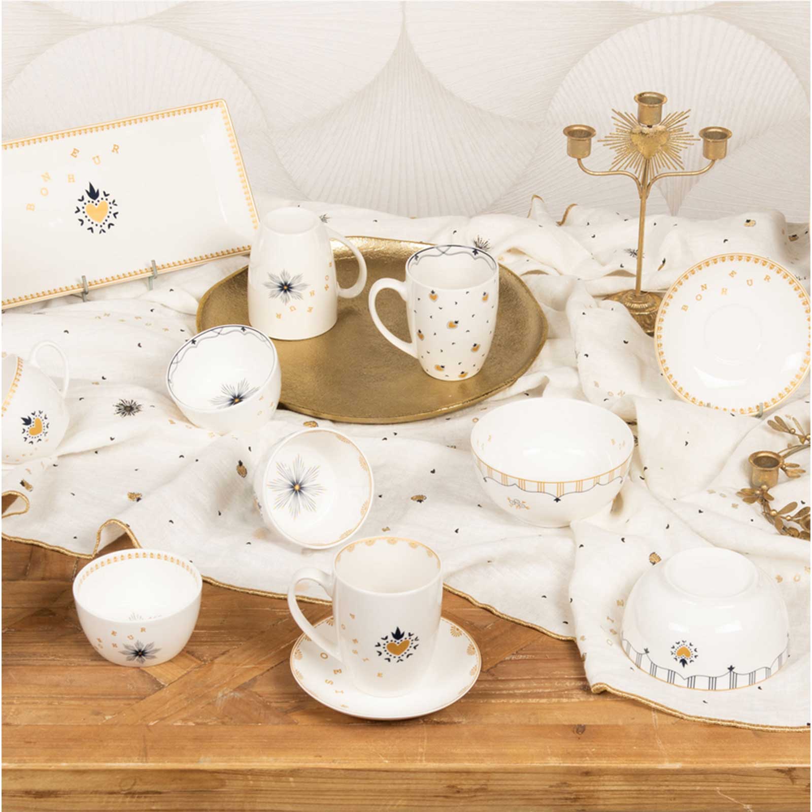 Ensemble de vaisselle en porcelaine blanche avec motifs dorés et bleu nuit, incluant des tasses, des soucoupes et des bols, disposés sur une nappe décorée